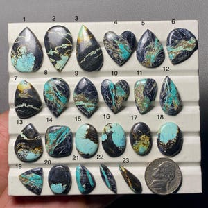May include: A collection of polished gemstones in various shapes, including teardrops, ovals, and hearts. The stones feature a mix of black, turquoise, and brown colors. A US nickel is included for size reference.