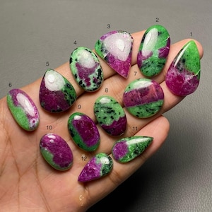 May include: A selection of twelve polished ruby zoisite gemstones in diverse shapes. The stones exhibit a blend of vivid green and deep magenta hues. Each stone features a unique pattern and cut, highlighting the natural beauty of the minerals.