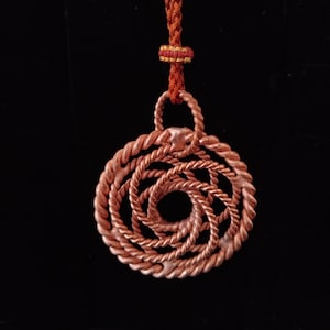 May include: A circular pendant crafted from twisted copper wire, featuring a spiral pattern that radiates from the center. The pendant is suspended from a braided reddish-brown cord, which includes a small decorative knot detail above the pendant.