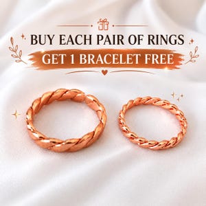 以下が含まれることがあります： ツイストロープのような質感の銅色のリング2点。上部には「BUY EACH PAIR OF RINGS GET 1 BRACELET FREE」というテキストが記載されています。リングは、星や葉などの装飾的なグラフィック要素が施された、柔らかいドレープ状の布地を背景に配置されています。