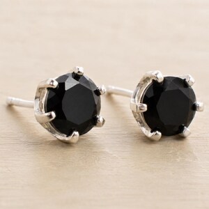 May include: A pair of stud earrings featuring round-cut black stones set in six-prong silver-toned metal settings. Each earring includes a straight post extending from the back of the setting, designed for pierced ears with a classic, secure mount.