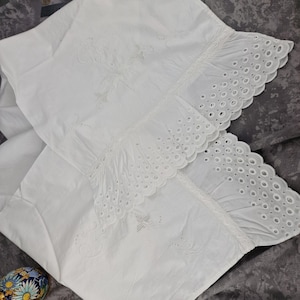 May include: Two white pillowcases with embroidered floral designs and eyelet lace trim. The pillowcases are made of a soft, white fabric and have a delicate, vintage aesthetic. The eyelet lace trim adds a touch of elegance to the bedding.