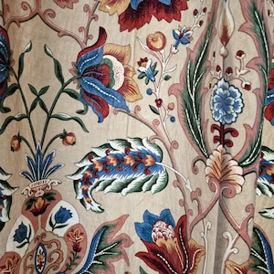 Könnte beinhalten: Nahaufnahme eines beigefarbenen Stoffes mit floralem Muster. Das Design zeigt große Blüten in Rot, Blau und Gelb, mit grünen Blättern und Stielen. Der Stil erinnert an Vintage-Textilien.