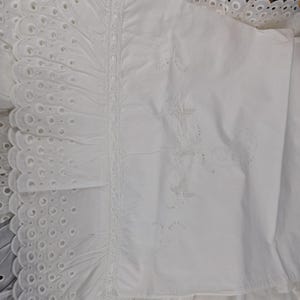 May include: White bedding with intricate embroidery and eyelet detailing. The image showcases a close-up of the fabric, highlighting the delicate patterns and textures. The design includes floral and geometric motifs, creating a classic and elegant look.