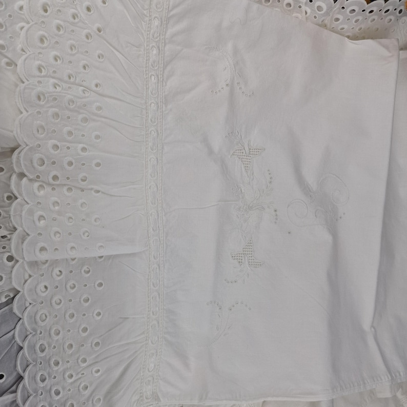 May include: White bedding with intricate embroidery and eyelet detailing. The image showcases a close-up of the fabric, highlighting the delicate patterns and textures. The design includes floral and geometric motifs, creating a classic and elegant look.