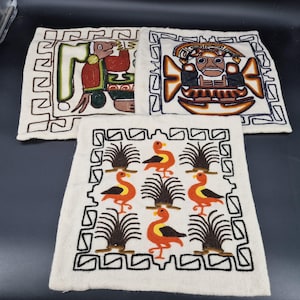 Peut inclure: Trois carrés textiles brodés avec des fonds crème. Les deux carrés supérieurs présentent des figures stylisées en rouge, marron et vert. Le carré inférieur affiche un motif d'oiseaux orange et de plantes brunes. Chaque carré a une bordure noire.