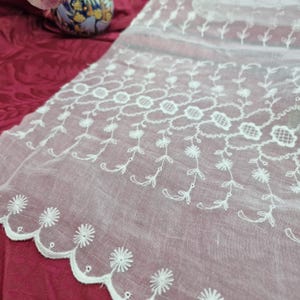 Peut inclure: Un chemin de table en tissu blanc transparent orné de broderies florales blanches complexes et d'un bord festonné. Le motif présente des vignes répétitives avec de petites fleurs et des éléments en grille circulaire sur toute la surface.