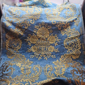 May include: Blue fabric featuring a gold floral pattern. The fabric has a damask design with large floral motifs and scrolling leaves. The edge is labelled with "GABRIELA" and "CLASSICS SEDA".