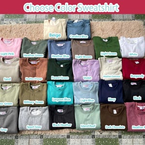 Op de afbeelding: Een verzameling sweatshirts in verschillende kleuren, waaronder beige, Carolina blauw, lichtroze, heidegroen en wit. De afbeelding toont een verscheidenheid aan tinten, met de tekst "Choose Color Sweatshirt" bovenaan.