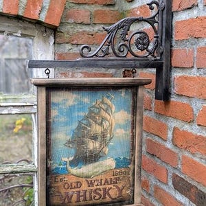 Könnte beinhalten: Vintage Holzschild für "Old Whale Whisky" mit einer Illustration eines Segelschiffs und eines Wals. Das Schild ist an einer dekorativen Metallhalterung an einer Backsteinmauer befestigt. Das Schild ist in einem rustikalen Holzrahmen gerahmt.