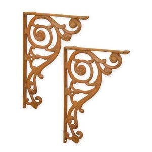 Op de afbeelding: Twee sierlijke, roestkleurige gietijzeren plankbeugels. Elke beugel heeft een decoratief krulontwerp met wervelende patronen en een platte bovenkant voor het ondersteunen van een plank. De beugels zijn ontworpen om aan een muur te worden bevestigd.