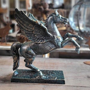 Könnte beinhalten: Bronzefarbene Pegasus-Statue mit ausgebreiteten Flügeln, stehend auf einem rechteckigen Sockel. Das Fabelwesen hat detaillierte Federn und einen fließenden Schweif. Dekorativer Artikel.