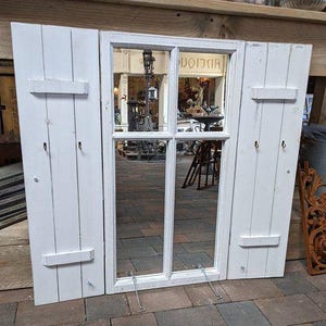 Peut inclure: Décor mural en bois blanc en forme de fenêtre avec deux volets. La fenêtre a une surface miroir et est divisée en quatre carreaux. Les volets ont des crochets et sont fixés avec des charnières. La pièce est conçue pour ressembler à une fenêtre avec des volets.