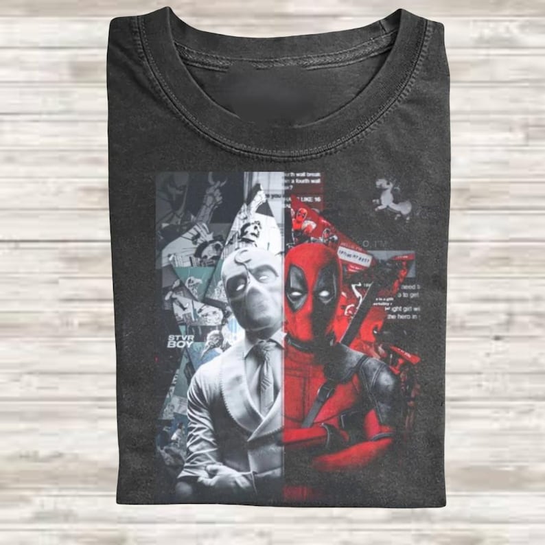 May include: A charcoal gray crew neck t-shirt featuring a split-face graphic design. The left side displays a white-masked character in a suit, while the right side shows a red-masked character. The background includes comic book style collage elements.