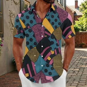 May include: A short-sleeved button-down shirt featuring a patchwork pattern of teal with black polka dots, purple with black swirls, yellow with a grid texture, and black with pink stripes. The shirt has a classic collar and white buttons.