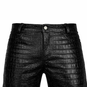 May include: Black leather shorts with a crocodile skin texture. The shorts have a button closure and belt loops. The garment is a dark, solid color and appears to be made of a durable material.