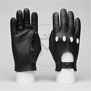 Könnte beinhalten: Paar schwarze Leder-Fahrhandschuhe. Die Handschuhe haben kleine Perforationen an den Fingern und am Handrücken zur Belüftung. Sie haben einen Riemen mit Knopfverschluss am Handgelenk und große kreisförmige Aussparungen.