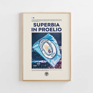 May include: Framed poster featuring a light blue flag with the Manchester City logo, waving in front of a stadium. The poster has the words "SUPERBIA IN PROELIO" in navy blue, with additional text at the top and bottom.