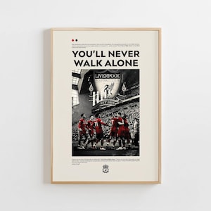 Op de afbeelding: Ingelijste poster met de tekst "YOU'LL NEVER WALK ALONE" en een zwart-wit afbeelding van een voetbalteam in het rood. Het logo van Liverpool Football Club is zichtbaar. De poster zit in een licht houten frame.