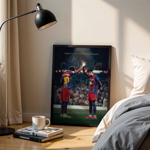 May include: A framed poster featuring two soccer players in red and blue uniforms, high-fiving each other. The poster is leaning against a wall next to a bed with gray bedding. The text on the poster reads: "Superhumans are real. They wear blaugrana."