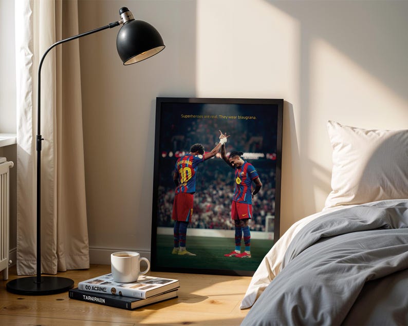 May include: A framed poster featuring two soccer players in red and blue uniforms, high-fiving each other. The poster is leaning against a wall next to a bed with gray bedding. The text on the poster reads: "Superhumans are real. They wear blaugrana."