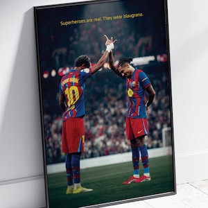 May include: Framed poster featuring two soccer players in blue and red uniforms, high-fiving on a green field. The jerseys have the number 10 on the back. Text at the top reads, "Superheroes are real. They wear blaugrana."