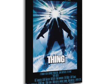 May include: A framed movie poster for "The Thing" features a silhouetted figure with a bright light emanating from its head. The title "THE THING" is prominently displayed in white, with the tagline "The ultimate in alien terror." The poster has a black border.