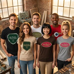 Pu&ograve; includere: Gruppo di persone che indossano magliette Von Dutch in vari colori, tra cui nero, bianco, beige, marrone e grigio. Ogni maglietta presenta il logo Von Dutch in diversi design. Lo sfondo include un muro di mattoni e strumenti da officina.