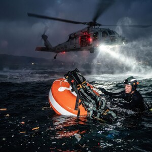 Könnte beinhalten: Eine nächtliche Rettungsszene mit einem Hubschrauber über unruhigem Wasser. Eine orange-weiße Boje mit Ausrüstung befindet sich im Wasser in der Nähe einer Person im Neoprenanzug. Der Scheinwerfer des Hubschraubers beleuchtet die Szene.