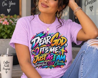 Op de afbeelding: Een lichtpaars t-shirt met korte mouwen en een kleurrijke grafische print met de tekst "Dear God, It's Me, Just As I Am, Imperfect. Still Chosen." Het ontwerp bevat levendige verfspatten, een hart en een kruis in diverse felle kleuren.