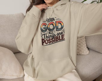 Op de afbeelding: Een beige hoodie met een grafische print op de borst met de tekst "With GOD All Things are POSSIBLE" in een retro lettertype. Het ontwerp bevat horizontale strepen in gedempte oranje, blauwe en donkerbruine kleuren.