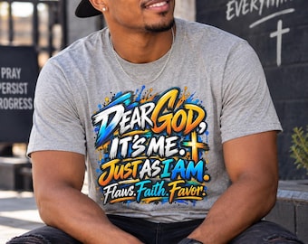 Op de afbeelding: Een grijs gemêleerd T-shirt met korte mouwen en een levendige, meerkleurige grafische print met de tekst "Dear God, It's Me. Just As I Am. Flaws. Faith. Favor." Het ontwerp bevat verfspatten, opvallende typografie en een kruissymbool.