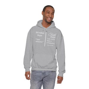 A man wearing a grey hoodie with text printed on it, smiling and looking to the side.