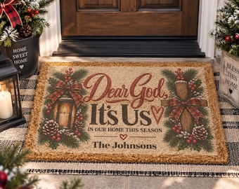 Op de afbeelding: Een rechthoekige beige kokosmat met een opdruk van een lantaarn, een kruis, dennentakken, rode bessen en dennenappels. De tekst luidt: Dear God, It's Us, IN OUR HOME THIS SEASON en The Johnsons, vergezeld door twee kleine hartjes als icoon.