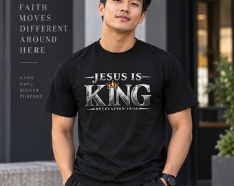 Op de afbeelding: Een zwart t-shirt met korte mouwen voorzien van de witte tekst "JESUS IS KING", een klein gouden kroonicoontje boven het woord "KING" en de tekst "REVELATION 19:16" eronder. Het shirt toont ook "FAITH MOVES DIFFERENT AROUND HERE".