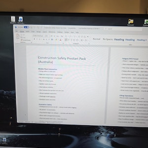 Puede incluir: Un monitor de computadora que muestra un documento de Microsoft Word titulado "Construction Safety Prestart Pack (Australia)". El documento incluye listas sobre la interacción de plantas móviles, seguridad de excavación, fatiga y operaciones de elevación.