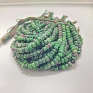 Könnte beinhalten: Ein Haufen grüner und roter Edelsteinperlen. Die Perlen sind klein, rund und facettiert, mit einer Mischung aus grünen und roten Farben. Die Perlen sind auf einer grün-roten Schnur aufgereiht.