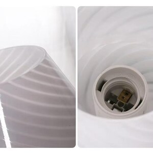 May include: A white glass lampshade with a swirled design. The lampshade has a bulb socket inside. The glass has a translucent quality, allowing light to pass through. The lampshade is designed for use with a light bulb.