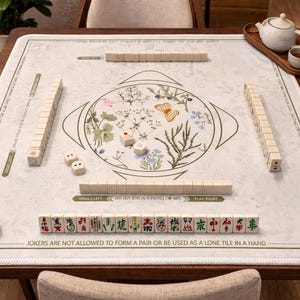 Puede incluir: Mesa de mahjong de madera con fichas, dados y servicio de té. La mesa presenta un diseño floral en el centro y texto en los bordes. Las fichas están dispuestas para jugar, con una tetera y una taza en una bandeja de madera.
