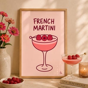 Puede incluir: Una lámina enmarcada con fondo rosa y el texto FRENCH MARTINI en letras de color rojo oscuro sobre una ilustración estilizada de un cóctel en una copa tipo cupé, decorado con tres frambuesas en un palillo de metal.
