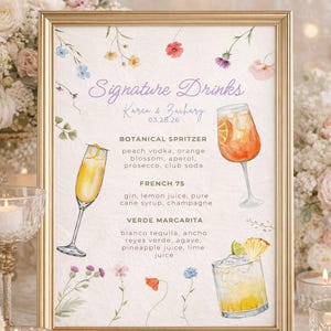 Może przedstawiać: Złota oprawiona tablica z napisem "Signature Drinks" i imionami "Karen & Zachary" z datą "03.28.26". Tablica zawiera trzy przepisy na koktajle: Botanical Spritzer, French 75 i Verde Margarita. Kwiatowe ilustracje i złota rama.