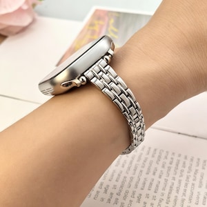 May include: A silver-toned smartwatch with a metallic link band featuring a multi-row design. The watch case has a smooth, rounded edge and a polished finish, while the bracelet consists of small, interconnected rectangular metal links.