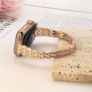 May include: A rose gold smartwatch with a matching metallic link band. The watch features a rectangular case with a side button and a digital crown. The band consists of small, polished rectangular links connected in a multi-row pattern.