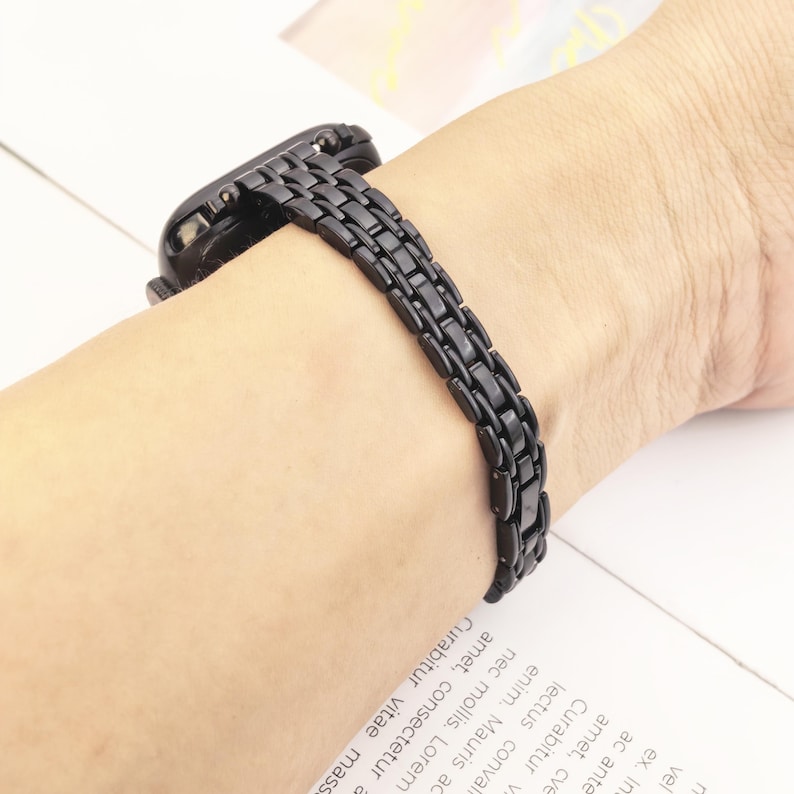 May include: A black metal watch band featuring a multi-link design with a polished finish. The strap is composed of small, rectangular interlocking segments that create a flexible and continuous chain structure, securely attached to a black watch case.