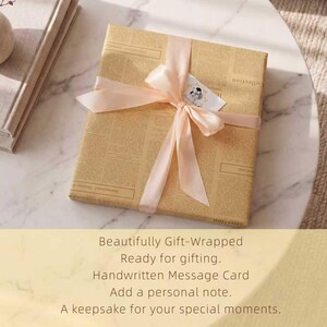 May include: A gift wrapped in tan newspaper print paper, tied with a light pink ribbon and bow. A small tag with a drawing is attached to the bow. The text on the gift wrap reads: "Beautifully Gift-Wrapped, Ready for gifting, Handwritten Message Card, Add a personal note, A keepsake for your special moments."