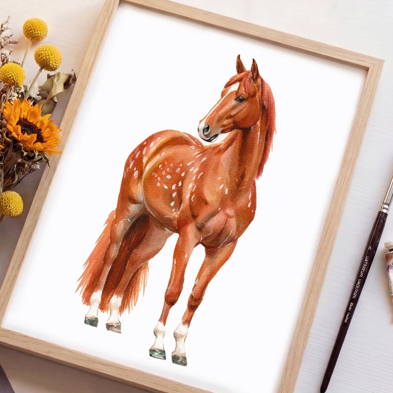 May include: Watercolor painting of a chestnut horse with white markings, set in a wooden frame. The horse is depicted in a dynamic pose, with its head turned and body angled. The artwork features detailed brushstrokes and a natural color palette.