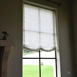 May include: A large window with a black grid frame and a striped, light-colored curtain. The curtain is pulled up, revealing a view of green grass outside. A black rod hangs above the window.