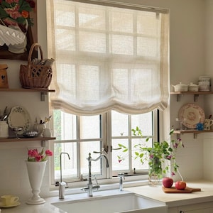 May include: A kitchen interior featuring a white sink, window, and work surface. A woven basket, vase of flowers, and apples on a chopping board add colour. A beige window blind is drawn up, allowing natural light.