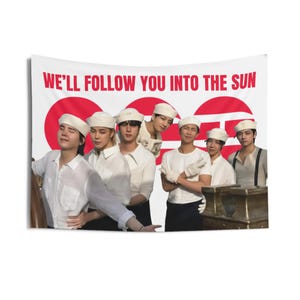 以下が含まれることがあります： 赤い文字で「WE'LL FOLLOW YOU INTO THE SUN」と書かれた白いタペストリー。白いシャツと帽子をかぶった人々のグループが、赤い円の前で立っています。人々は互いに近くに立っています。