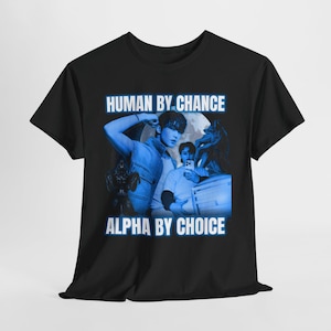 May include: Black t-shirt with a blue graphic design. The design includes the text "HUMAN BY CHANCE" and "ALPHA BY CHOICE". The graphic also features images of people and a wolf.